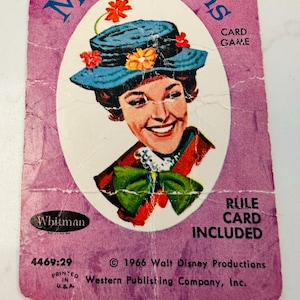 May include: Vintage Mary Poppins card game card. The card features an illustration of Mary Poppins wearing a blue hat with flowers. The card is purple with the text "Mary Poppins" and "Card Game". The card is from 1966.