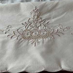 May include: Cream-colored fabric with embroidered floral and circular lace design. The embroidery features a central flower with surrounding leaves and delicate circular patterns. The bottom edge has a scalloped trim.