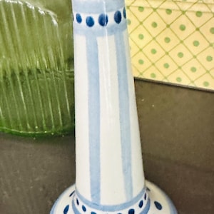 May include: A white ceramic candlestick holder featuring a tapered cylindrical body decorated with vertical light blue stripes and horizontal bands of dark blue dots around the flared top rim and the circular base of the object.