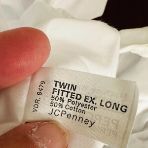 May include: A white fabric tag with black text, reading "TWIN FITTED EX. LONG" and "50% Polyester 50% Cotton." The tag also includes the brand "JCPenney" and the number "VDR. 9479."