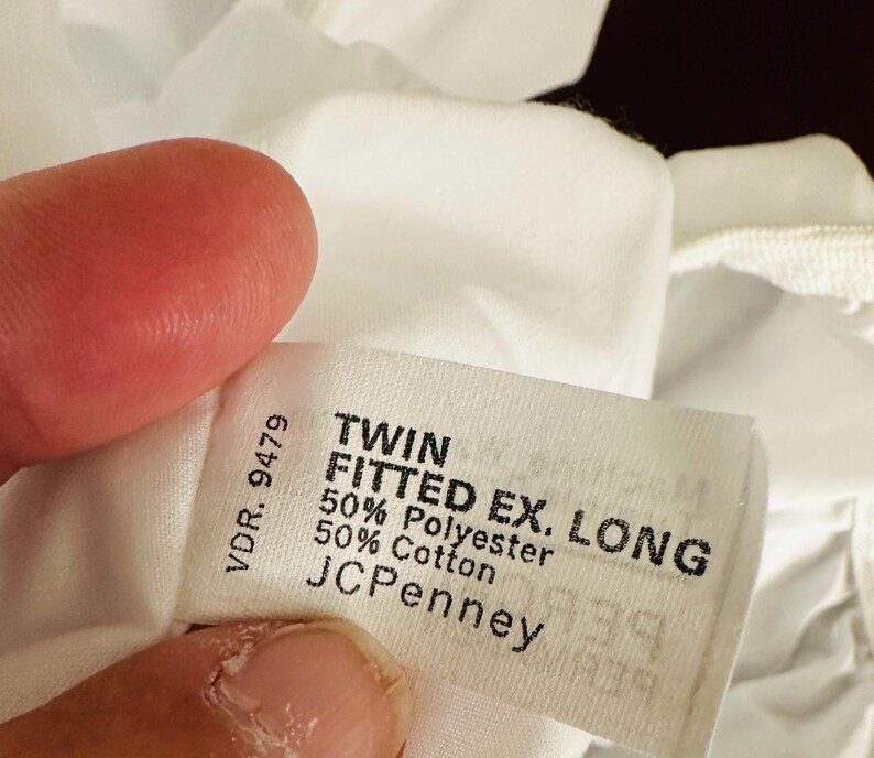 May include: A white fabric tag with black text, reading "TWIN FITTED EX. LONG" and "50% Polyester 50% Cotton." The tag also includes the brand "JCPenney" and the number "VDR. 9479."