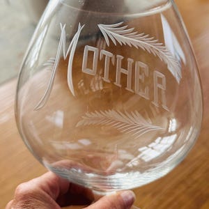 May include: A white ceramic mug with a black handle and the text "But First, Coffee" in a black, handwritten-style font. The mug is on a white surface.