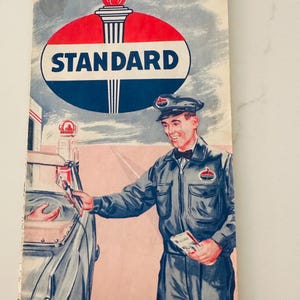 May include: Vintage brochure for Standard Oil Company, featuring a service station attendant in a blue uniform. The brochure's cover displays the Standard logo with a red, white, and blue color scheme, and the text "Central United States."