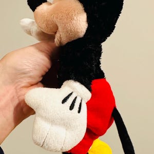 Puede incluir: Un peluche de Mickey Mouse, con cabeza y orejas negras, cara beige y guantes blancos. El juguete tiene pantalones cortos rojos y zapatos amarillos. El juguete mide aproximadamente 30 cm de alto.