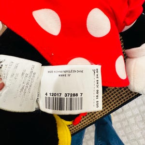 May include: A Minnie Mouse plush doll with a red bow featuring white polka dots. The tag reads "MADE IN CHINA/FABRIQU&Eacute; EN CHINE MINNIE 15". The doll is black, red, and white.