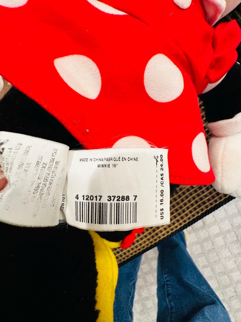 May include: A Minnie Mouse plush doll with a red bow featuring white polka dots. The tag reads "MADE IN CHINA/FABRIQU&Eacute; EN CHINE MINNIE 15". The doll is black, red, and white.