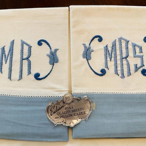 May include: Two white pillowcases with blue embroidered initials "MR" and "MRS". The pillowcases have a blue border and a decorative tag that reads "Exclusive Fine Quality Sheets and Pillow Cases".