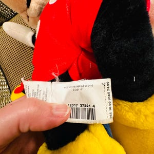 May include: A plush Mickey Mouse toy, featuring a red jacket with white polka dots, black gloves, and a yellow body. The tag reads "MICKEY 15" and "MADE IN CHINA".