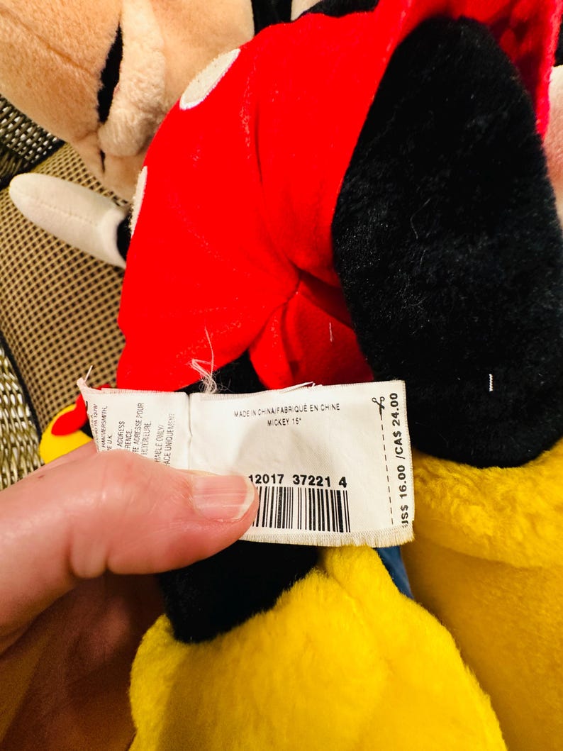 May include: A plush Mickey Mouse toy, featuring a red jacket with white polka dots, black gloves, and a yellow body. The tag reads "MICKEY 15" and "MADE IN CHINA".