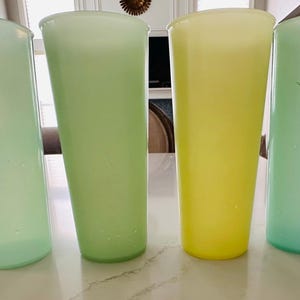 May include: Four tall, vintage-style drinking glasses in shades of green and yellow are arranged on a white surface. The glasses have a slightly tapered shape and a smooth, translucent appearance, perfect for serving beverages.