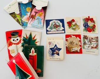 May include: A collection of vintage Christmas cards and gift tags. The cards feature illustrations of snowmen, angels, candles, and winter scenes. The color palette includes red, green, blue, and gold. Some tags have a "Merry Christmas" message.