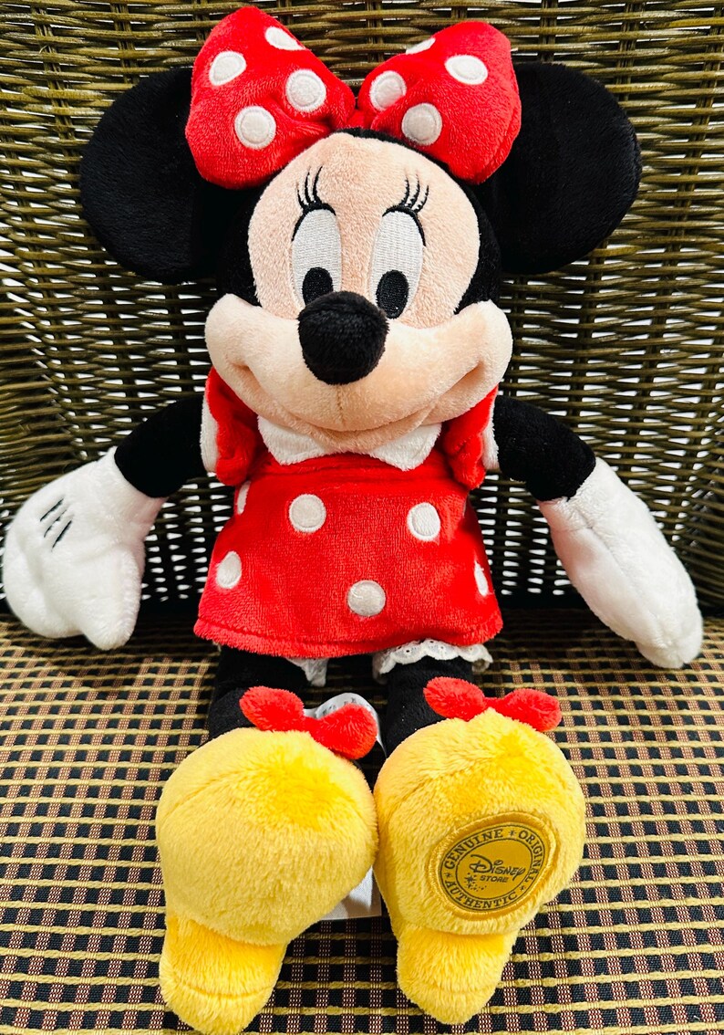 Puede incluir: Mu&ntilde;eca de peluche de Minnie Mouse, con un vestido rojo con lunares blancos, un lazo a juego y zapatos amarillos. La mu&ntilde;eca tiene orejas negras, una nariz negra y guantes blancos. Los zapatos tienen un logotipo de Disney Store.
