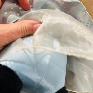K&ouml;nnte beinhalten: Nahaufnahme einer Pl&uuml;schpuppe, die ein hellblaues Kleid mit silbernen Pailletten tr&auml;gt. Das Kleid hat einen wei&szlig;en, durchsichtigen &Uuml;berzug. Der schwarze Fu&szlig; der Puppe ist unten im Bild zu sehen.