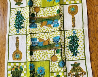 May include: A vintage kitchen towel with a repeating pattern of kitchen utensils, flowers, and decorative items in green, blue, and gold. The towel has a white background with a grid of squares and floral accents, creating a retro aesthetic.