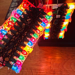 May include: A set of colorful Christmas lights with various colored bulbs, including red, blue, green, and yellow. The lights are strung together with black wiring and are arranged in a tray. The image is taken indoors.