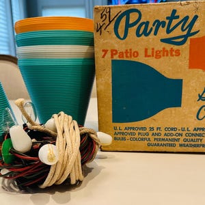 May include: An image of vintage party supplies. Two turquoise and orange planters, a bundle of lights, and a box of 7 patio lights. The box reads "Hay and Colorful" and "Guaranteed Weatherproof".