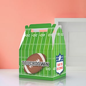 Op de afbeelding: Groene en witte cadeaudoos met een voetbalveldontwerp. De doos heeft een voetbalafbeelding en de tekst "TOUCHDOWN". De doos heeft ook een blauw-wit schild met sterren en de tekst "BEDANKT VOOR JE KOMST!"