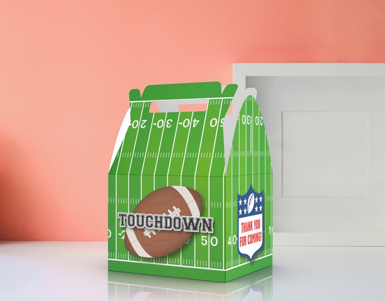 Op de afbeelding: Groene en witte cadeaudoos met een voetbalveldontwerp. De doos heeft een voetbalafbeelding en de tekst "TOUCHDOWN". De doos heeft ook een blauw-wit schild met sterren en de tekst "BEDANKT VOOR JE KOMST!"