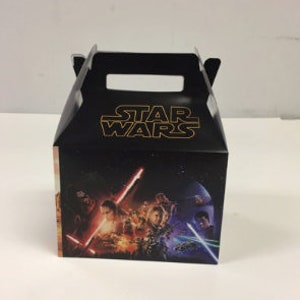 May include: A black and gold Star Wars themed party favor box with a picture of characters from the movie on the front.