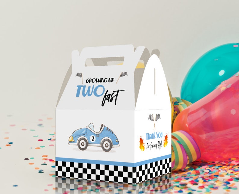 May include: A white favor box with a blue race car design. The box has a handle and says "Growing Up Two Fast" on the front. The back of the box says "Thank You for Racing By!"