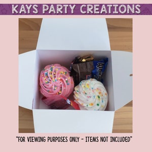 Op de afbeelding: Een witte doos met een roze en witte cupcake, een witte cupcake met sprinkles en een chocolade reep erin. De doos is open en de items zijn zichtbaar. "Alleen voor kijkdoeleinden - items niet inbegrepen" staat onderaan de afbeelding.