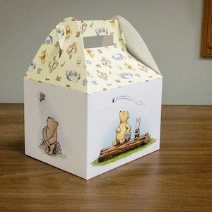May include: A Winnie the Pooh themed gift box with a handle. The box is white with a yellow and white pattern of Winnie the Pooh characters. The front of the box features Winnie the Pooh and Piglet sitting on a log.