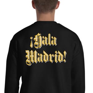 May include: Black sweatshirt with the text "¡Hala Madrid!" in gold lettering. The text is in a decorative font. The sweatshirt is a crew neck style.