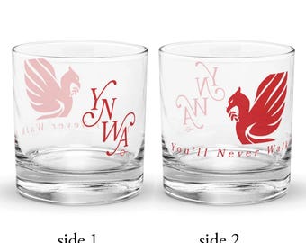 May include: Two clear glass tumblers featuring red graphics. One side displays a red bird emblem and the text YNWA in a stylized font. The other side shows the same bird emblem with the text You'll Never Walk Alone printed in a thin red font.