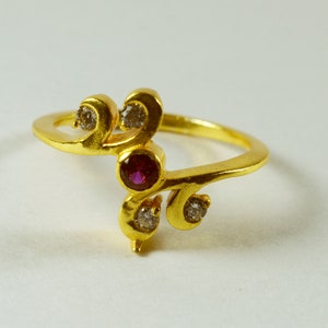 May include: A gold ring with a delicate, swirling design. The ring features a single red gemstone and several smaller clear gemstones.