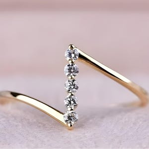 Può includere: Un anello d'oro con una fila di cinque diamanti trasparenti incastonati in una fascia a forma di V.