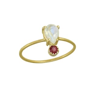 May include: A gold ring featuring a teardrop-shaped moonstone and a small red gemstone.