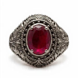 May include: A silver ring with a large, oval-cut, deep red gemstone. The ring has detailed, ornate patterns around the stone and on the band, giving it a vintage appearance. The ring is displayed on a white background.