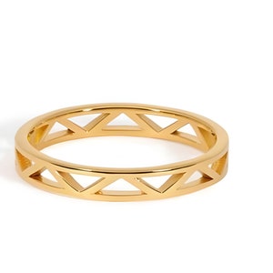 Könnte beinhalten: Ein goldfarbener Ring mit geometrischem Design. Der Ring hat eine Reihe offener Dreiecke um das Band. Der Ring ist vor einem weißen Hintergrund platziert, was seine polierte Oberfläche hervorhebt. Dieser Ring ist ein Schmuckstück.
