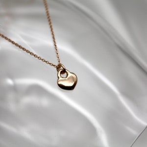 Könnte beinhalten: Eine zarte goldene Halskette mit einem kleinen Herz-Anhänger. Das Herz hat eine kleine Öffnung oben.
