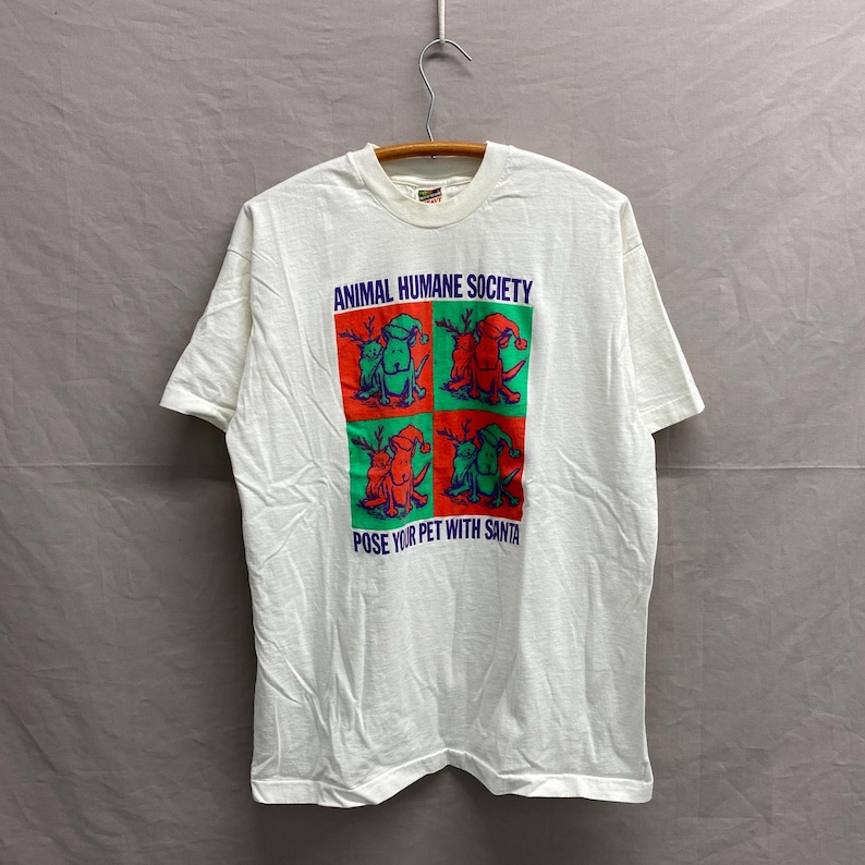 May include: White t-shirt with a green and red graphic of dogs wearing Santa hats. The text "Animal Humane Society" and "Pose Your Pet With Santa" are printed on the shirt.