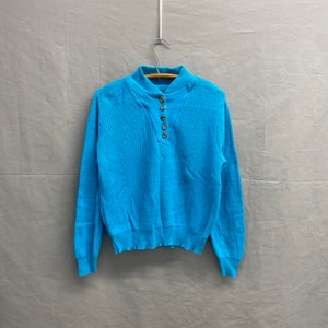 May include: A bright blue long-sleeved sweater with a mock neck and a button placket.