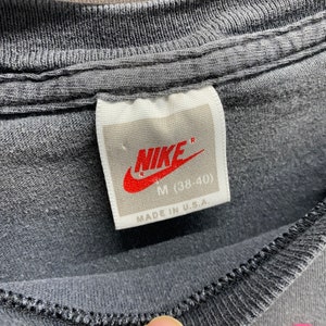 May include: A white tag with black text that reads "NIKE" with a red swoosh logo. The tag also says "M (38-40)" and "MADE IN U.S.A."