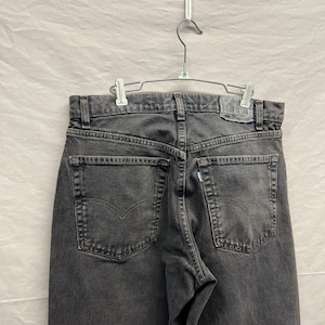 May include: Back view of black denim jeans hanging on a metal hanger. The jeans have two back pockets with a curved design and a small, rectangular label that reads "silver tab".