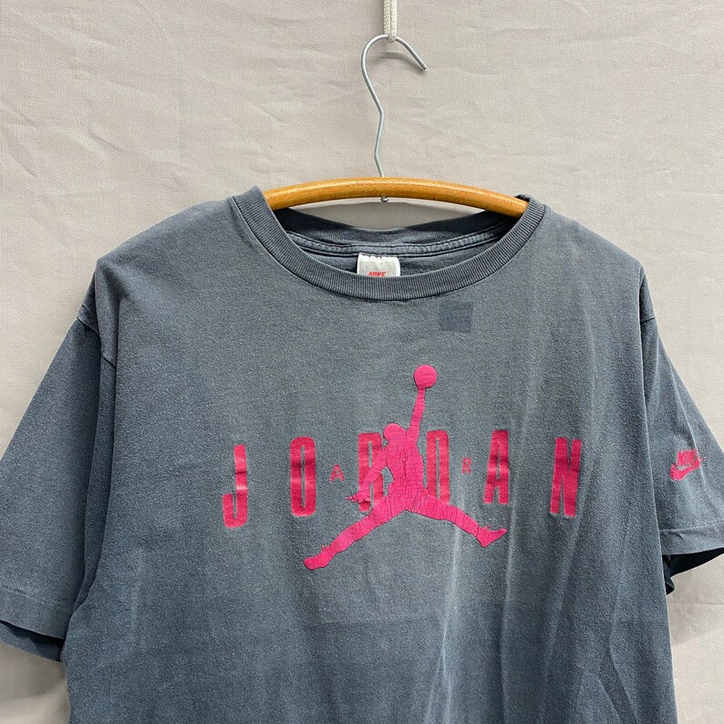 May include: A grey t-shirt with a pink Jordan logo and the word "JORDAN" printed on the front.