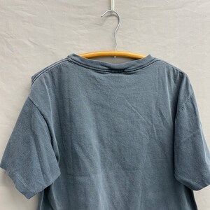 May include: A dark grey t-shirt with a crew neck and short sleeves. The shirt is hanging on a wooden hanger.
