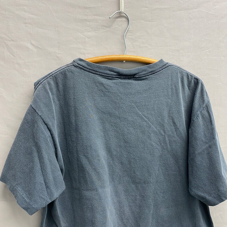 May include: A dark grey t-shirt with a crew neck and short sleeves. The shirt is hanging on a wooden hanger.