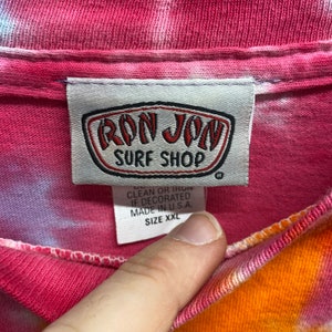May include: A pink, orange, and white tie-dye t-shirt with a white tag that says "Ron Jon Surf Shop" and "Size XXL".