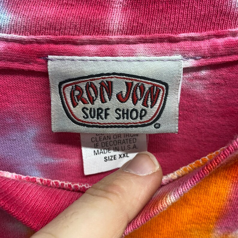 May include: A pink, orange, and white tie-dye t-shirt with a white tag that says "Ron Jon Surf Shop" and "Size XXL".