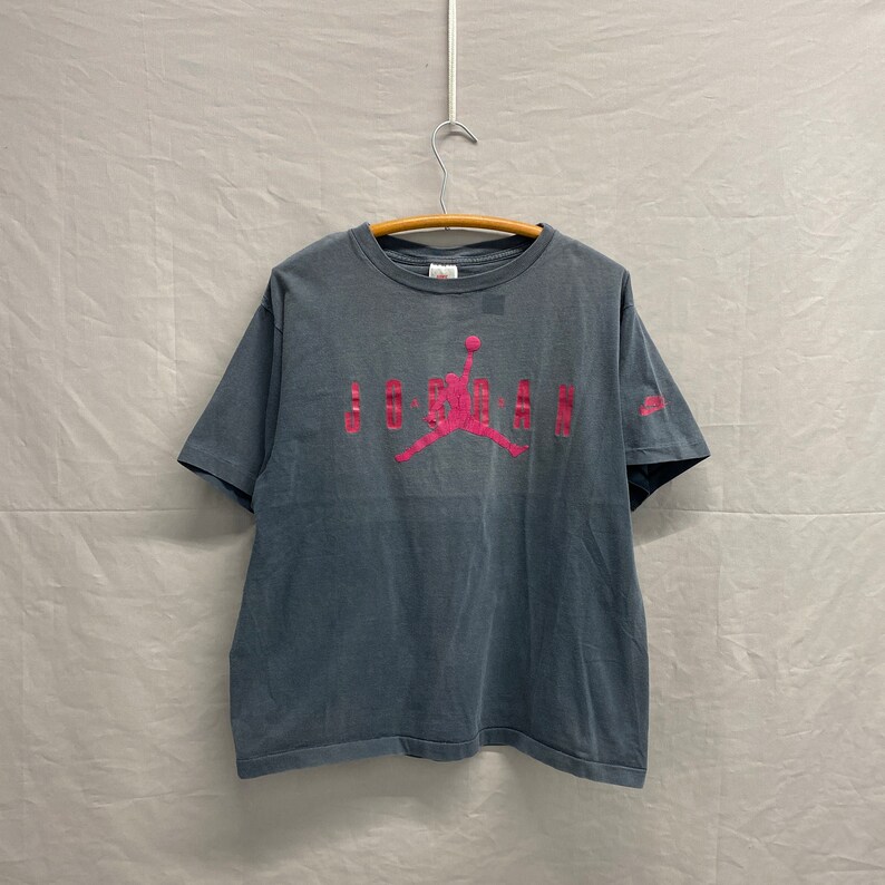 May include: A vintage grey t-shirt with a pink Jordan logo and the word "JORDAN" printed on the front.