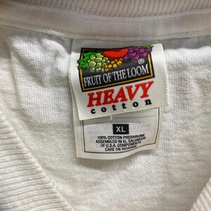 May include: White Fruit of the Loom t-shirt tag with the words "Heavy Cotton" in red and "XL" in black. The tag also includes the text "100% Cotton Preshrunk Assembled in El Salvador of U.S.A. Components Care on Reverse."