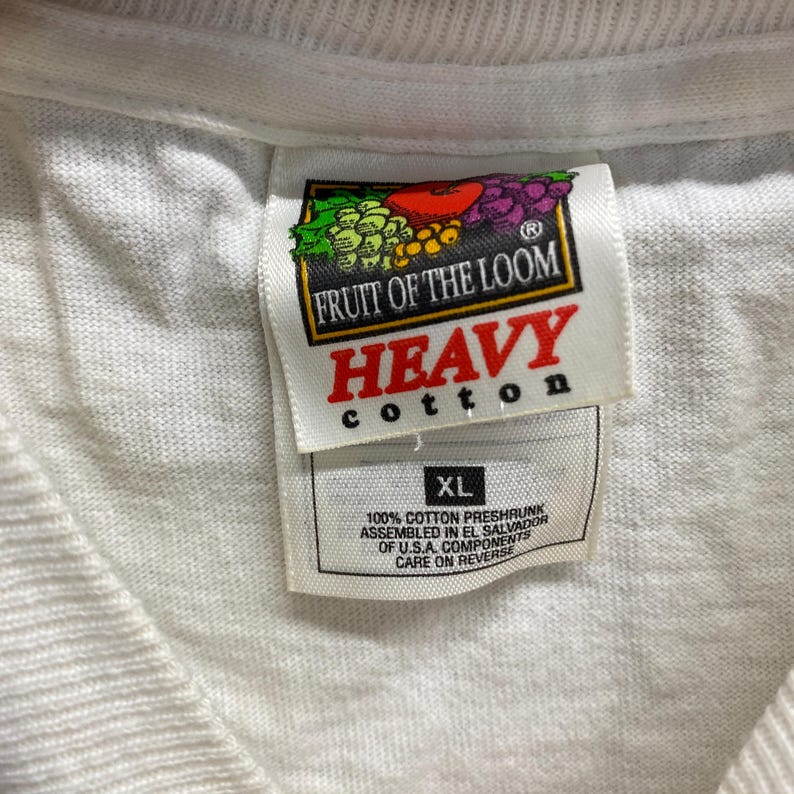 May include: White Fruit of the Loom t-shirt tag with the words "Heavy Cotton" in red and "XL" in black. The tag also includes the text "100% Cotton Preshrunk Assembled in El Salvador of U.S.A. Components Care on Reverse."