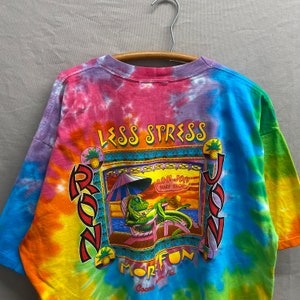 May include: A tie-dye t-shirt with a colorful graphic of a lizard lounging on a beach chair. The graphic includes the text "Less Stress More Fun" and "Ron Jon Surf Shop".