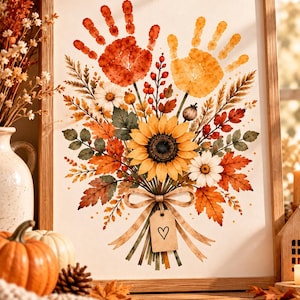 Peut inclure: Une impression d'art encadrée représentant un bouquet de fleurs et de feuillages d'automne, surmonté de deux empreintes de mains orange et jaune. Le bouquet inclut un tournesol central, des marguerites et des baies, noué par un ruban et une étiquette avec un cœur.