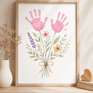 May include: Watercolour print of a bouquet featuring pink handprints as flowers. The bouquet includes lavender, yellow, and pink flowers, tied with a beige ribbon. The artwork is framed in a light brown wooden frame.