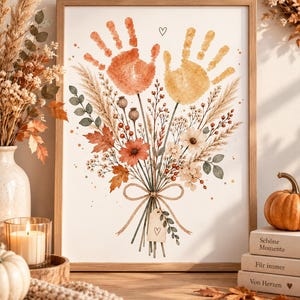 Op de afbeelding: Een ingelijste kunstprint met een aquarelillustratie van een boeket gedroogde bloemen en grassen. Twee handafdrukken, één in oranje en één in geel, staan bovenaan. Een klein label met een getekend hartje hangt aan de samengebonden stelen.